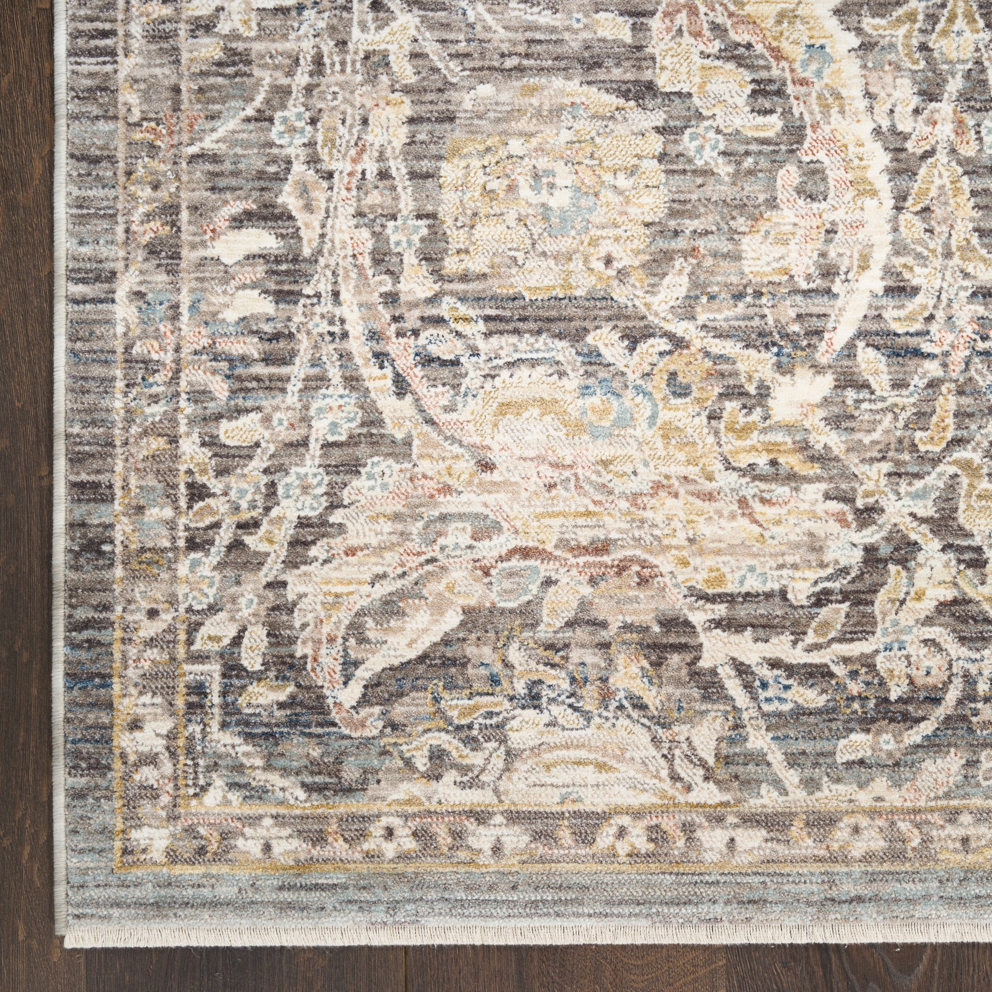 Close-up of a gray ornate oriental rug with beige, ivory and pale blue florals and border on a dark wood floor.