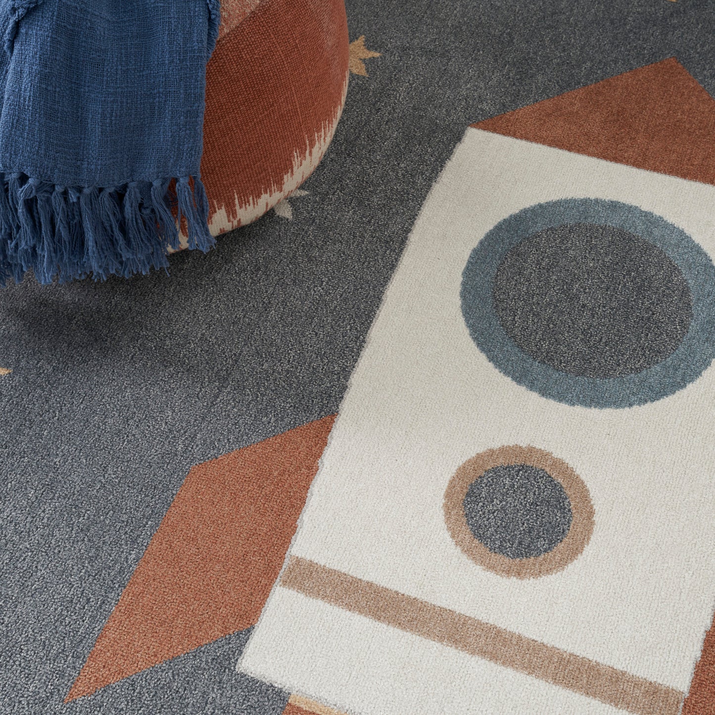 Blue fringed throw draped over a mid-century rug with beige, brown and blue geometric shapes and circular motifs.