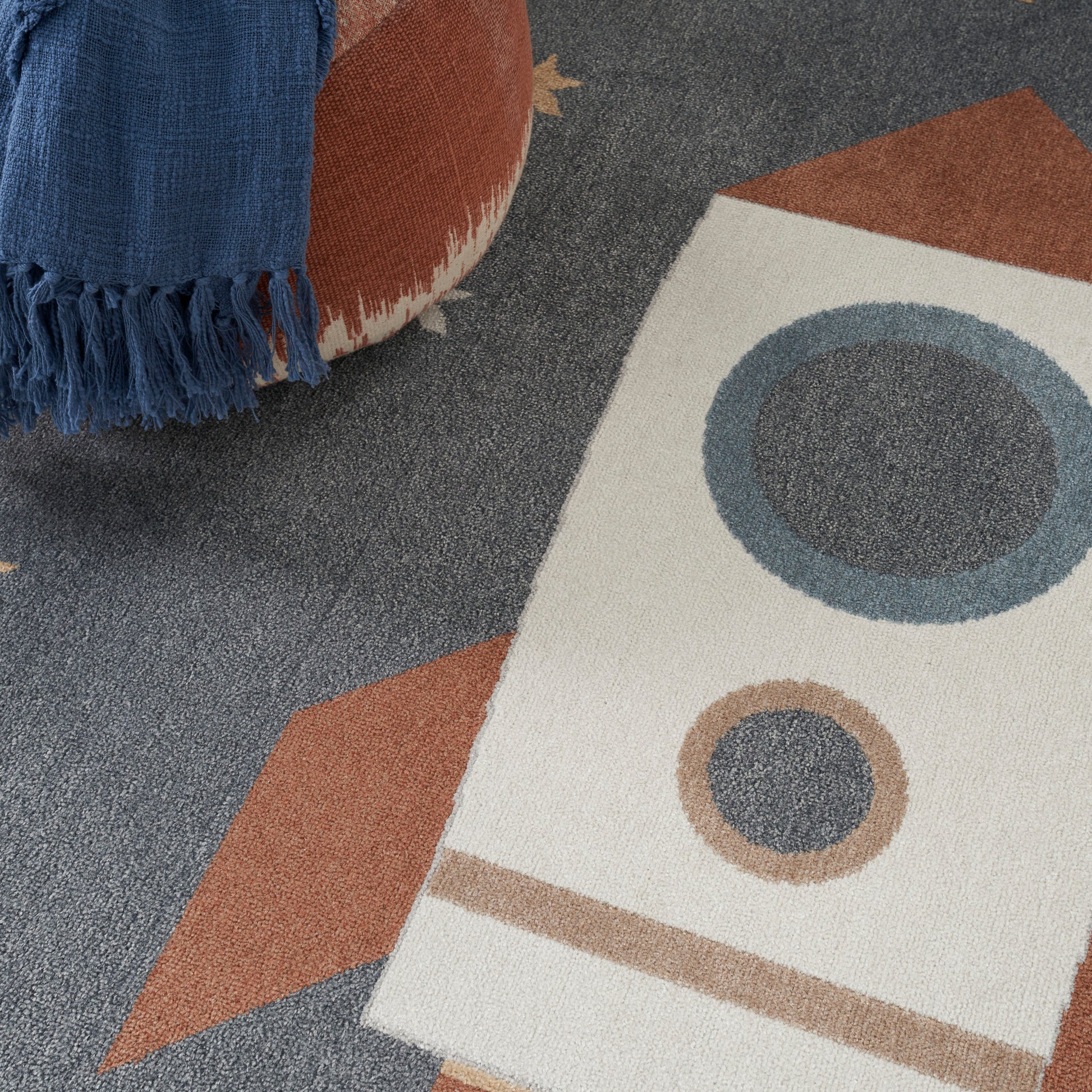 Blue fringed throw draped over a mid-century rug with beige, brown and blue geometric shapes and circular motifs.