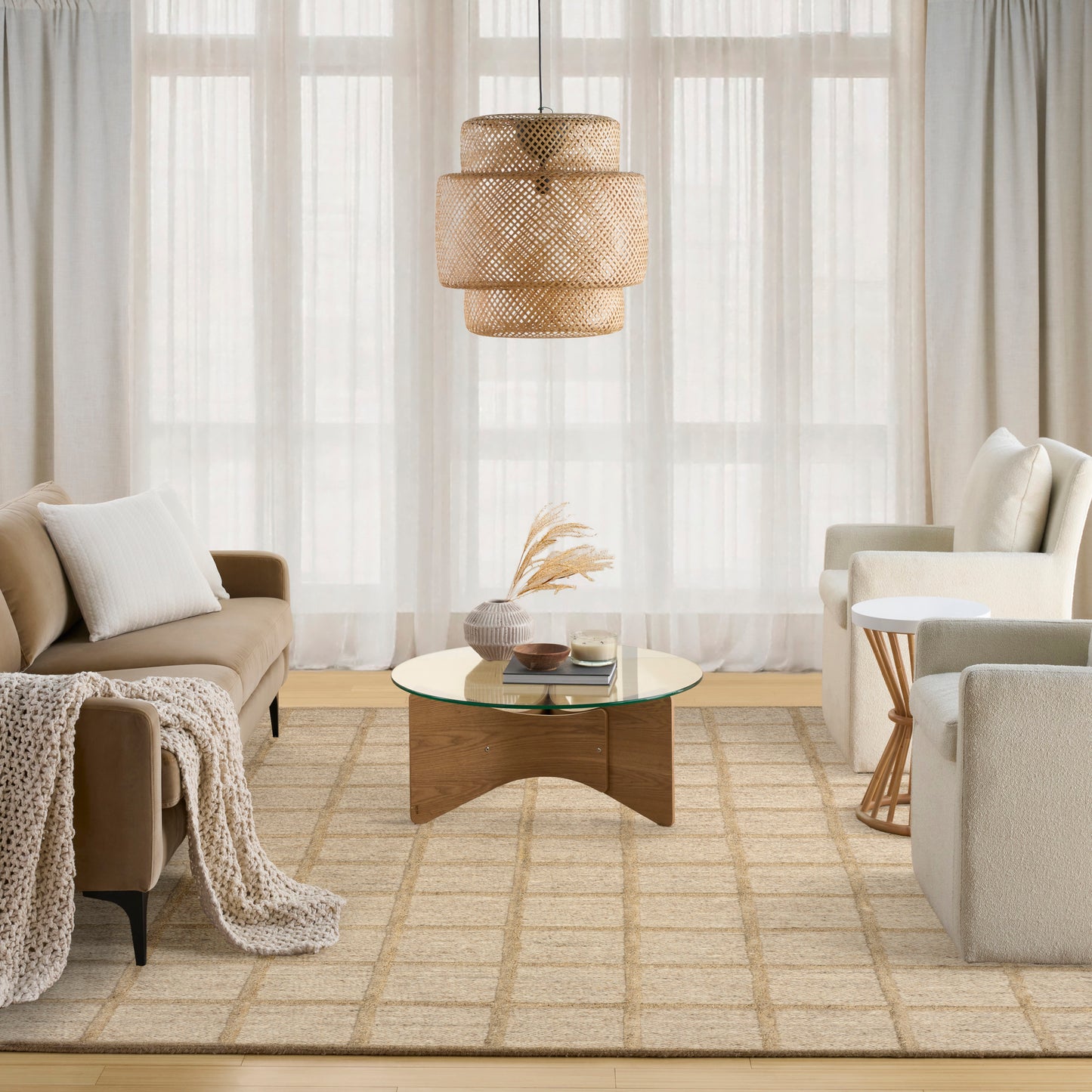 Neutral boho living room with beige sofa, light-gray seating, glass coffee table on a woven beige rug, rattan pendant light.