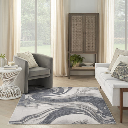 Abstract blue-gray swirl rug in a bright living room with gray armchair, light sofa, wicker cabinet, and plant.