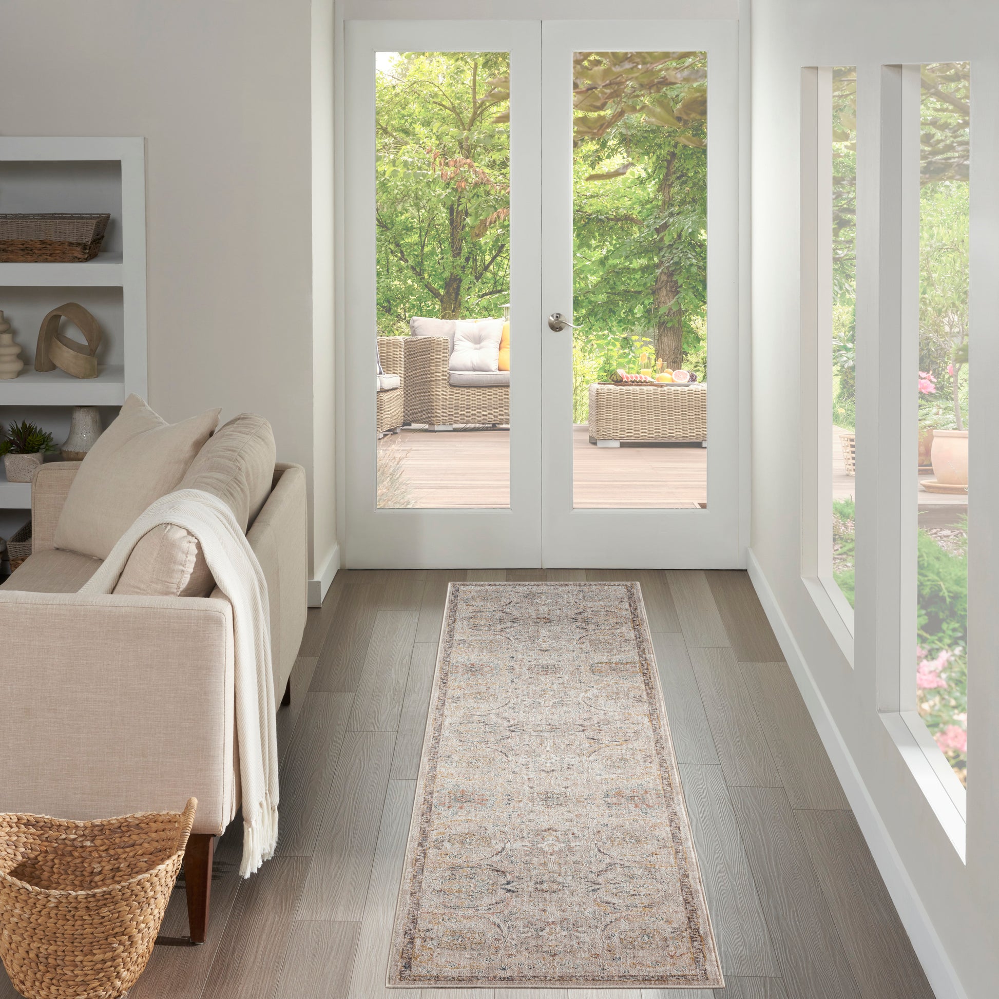 Bright living room with beige rug runner, light wood floors, cream sofa, white shelves, and glass doors to a garden deck.