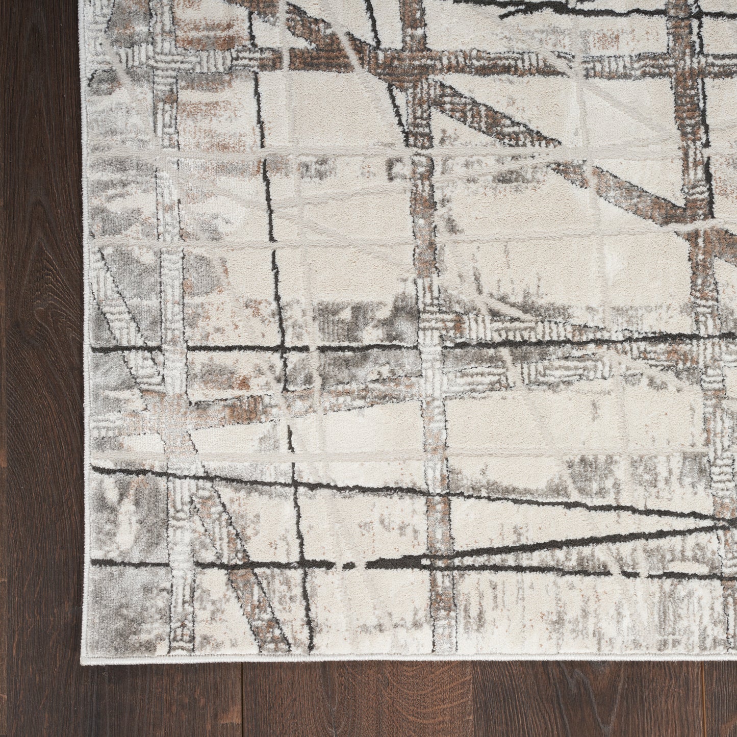 Modern abstract area rug in beige, ivory, gray and brown with grid-line geometric pattern on dark wood floor.