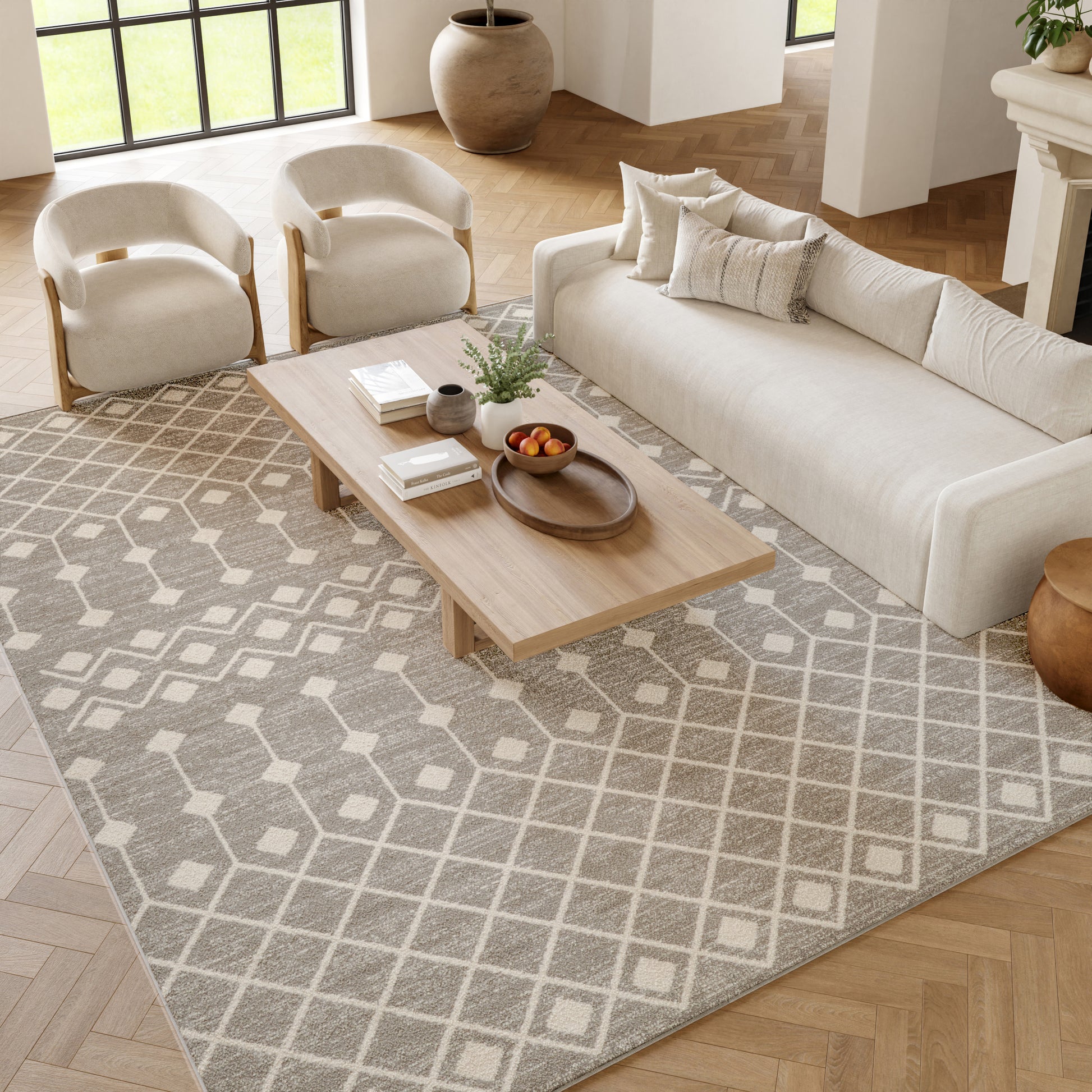 Cream sofa with two armchairs, light wood coffee table on a gray geometric rug; plants and fruit bowl.