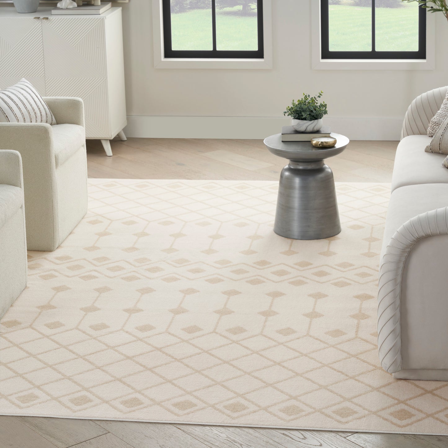 Cream living room with a beige geometric-pattern rug, light sofas, and a small gray round-top side table with a plant.
