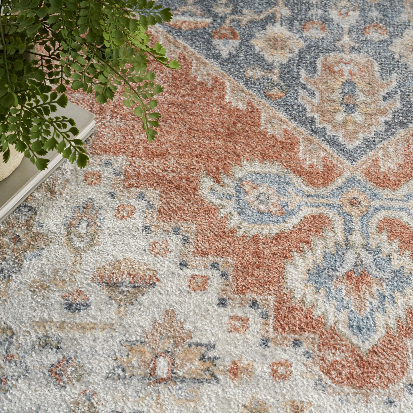 Oriental-style rug in rust orange, blue and ivory with floral medallions; green plant and books at edge.