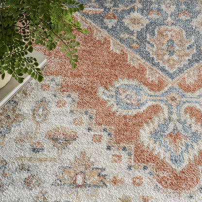 Oriental-style rug in rust orange, blue and ivory with floral medallions; green plant and books at edge.