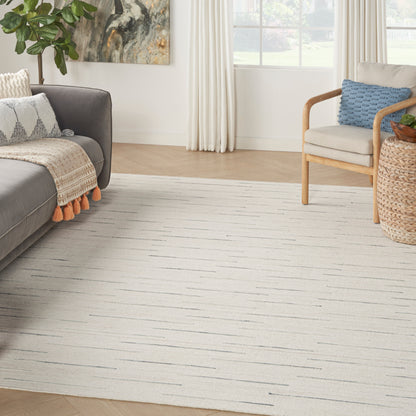 Cozy living room with cream striped area rug, gray sofa, wooden armchair, blue cushion, woven basket side table, and plants.