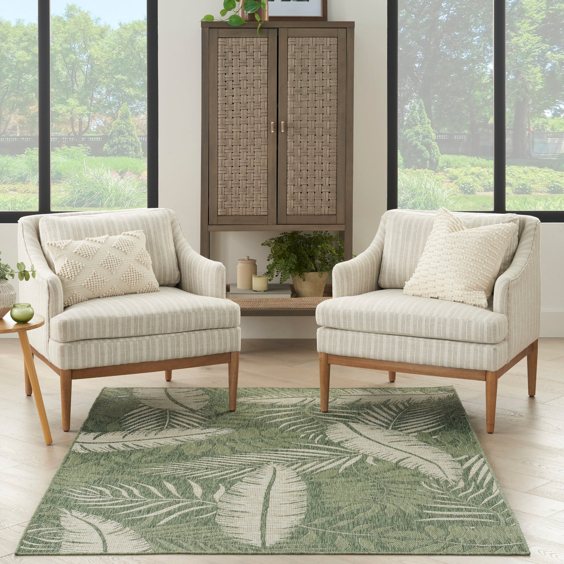 Outdoor rug 5' x 7' on a patio with two beige striped chairs, wooden legs, and a wicker cabinet.