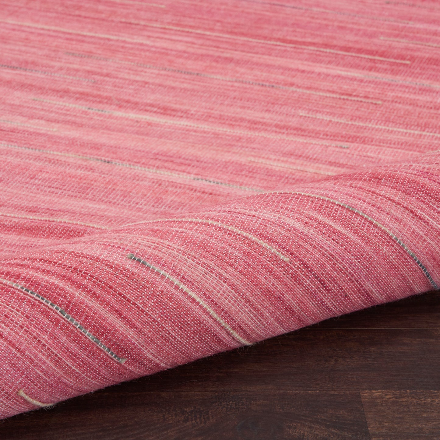 Pink woven rug with subtle white and gray stripes, folded edge on dark wood floor.