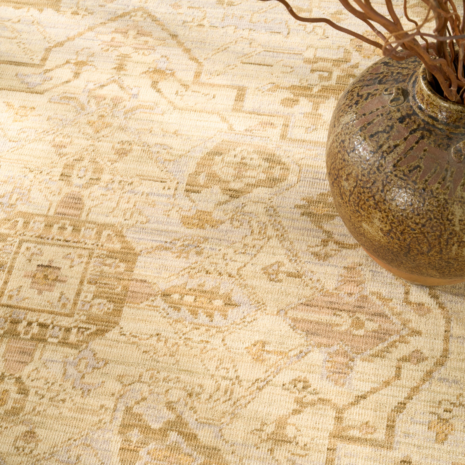 Beige patterned rug with subtle geometric motifs; rustic brown ceramic vase with dried twigs in the corner.