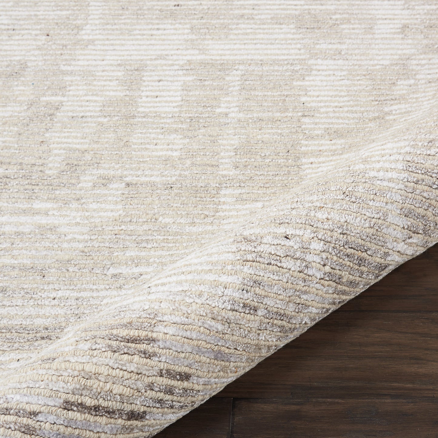 Beige area rug with subtle tonal pattern, rolled edge, plush pile on dark wood floor.
