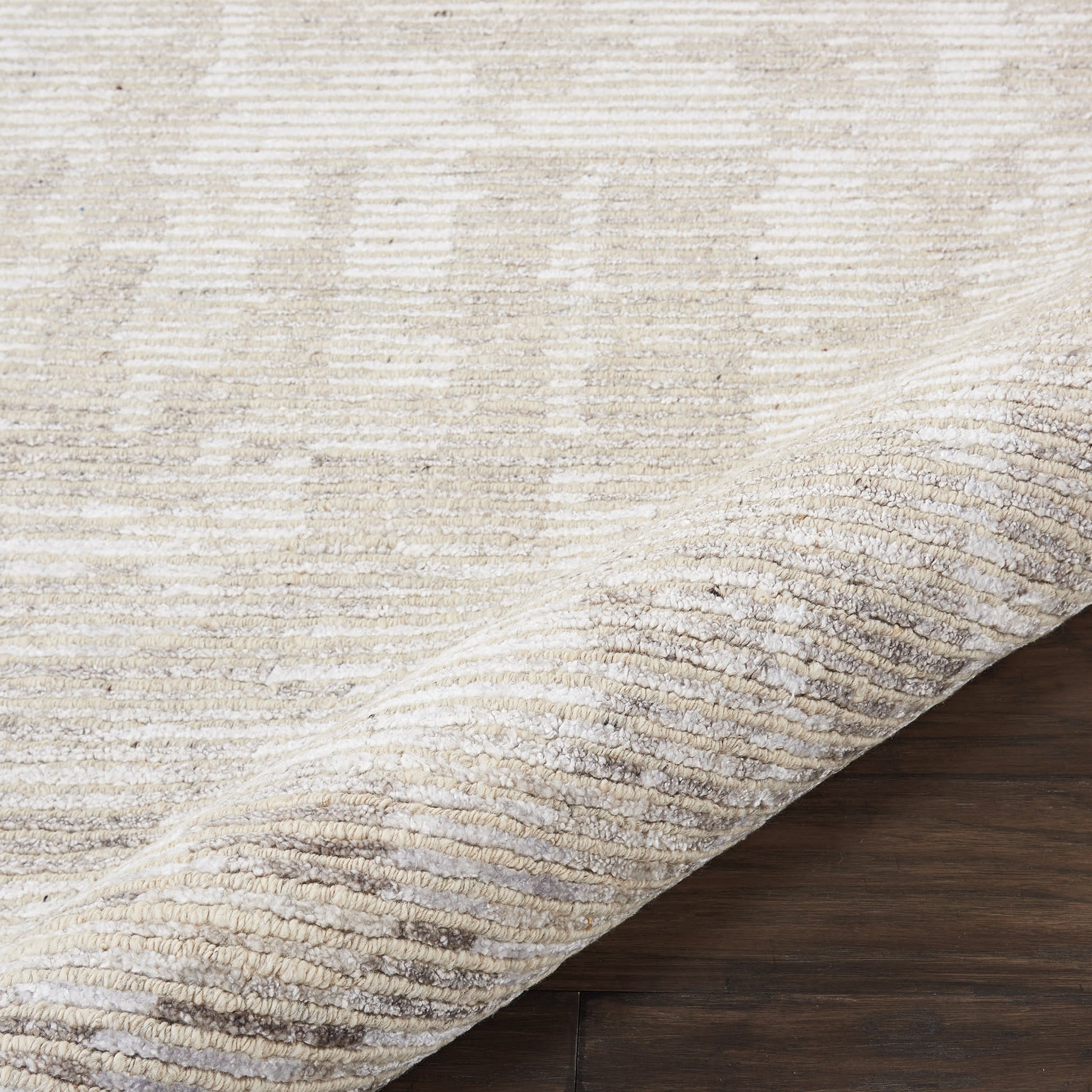 Beige area rug with subtle tonal pattern, rolled edge, plush pile on dark wood floor.