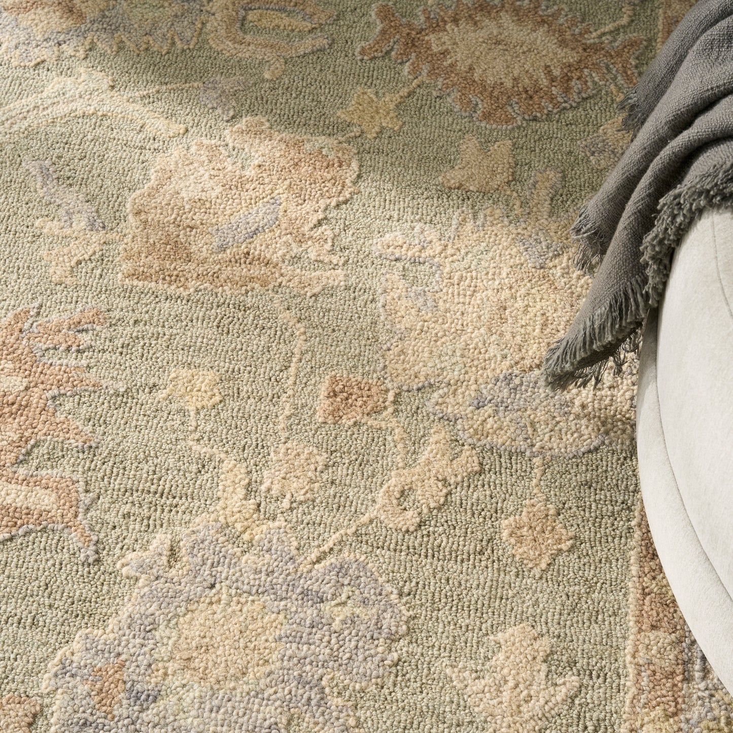 Muted floral-pattern area rug in sage green, beige and lavender with a soft textured pile; gray blanket draped nearby.