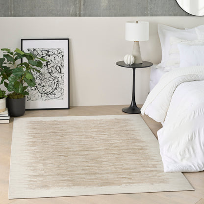 Beige rug on light wood floor, white bedding, black pedestal table with white lamp, framed abstract art, potted plant.