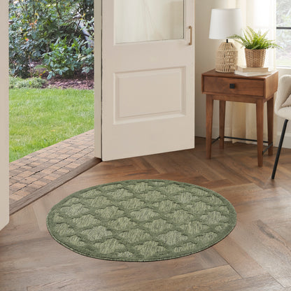 Round green quilted rug on wooden floor by an open door; entryway with a wooden table, lamp, and plant.