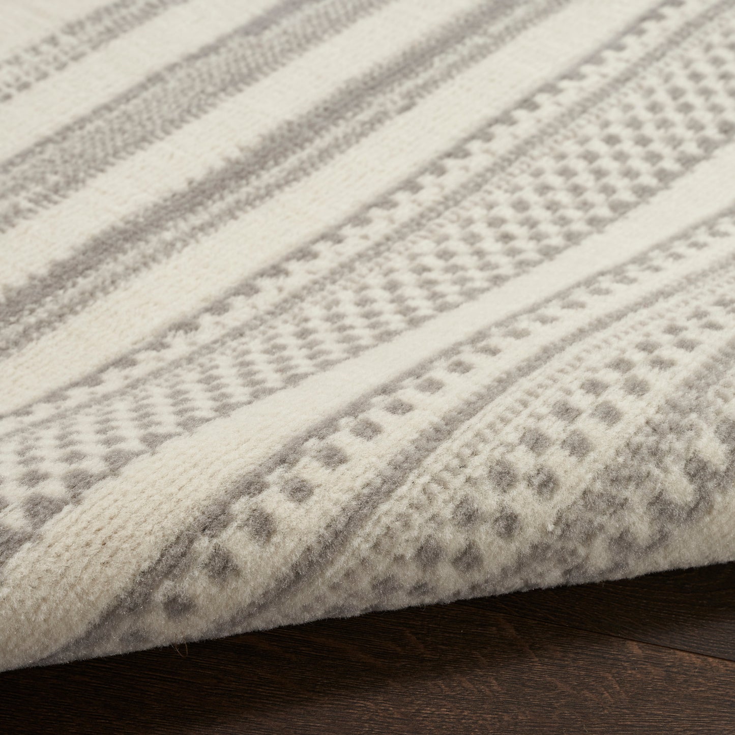 Cream and gray striped woven rug with geometric patterns, soft textured fabric folded on dark wood floor.