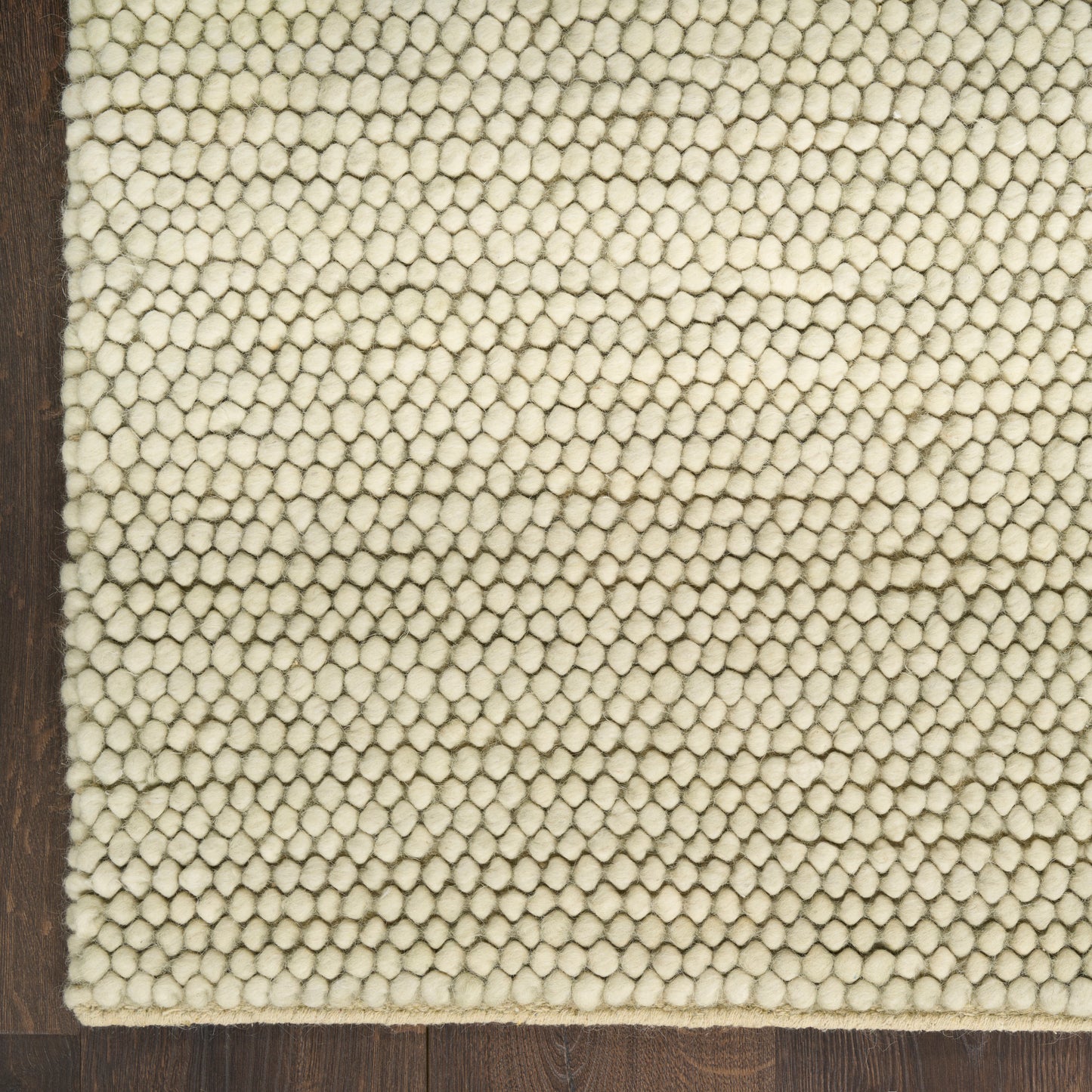 Ivory loop-pile rug with dense small tufts on dark wood floor; rectangular Berber-style decor.