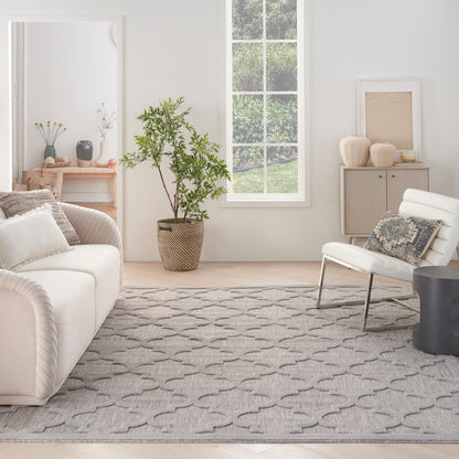 Neutral living room with white sofa, lounge chair, gray geometric rug, tall potted plant, and pale wood accents.