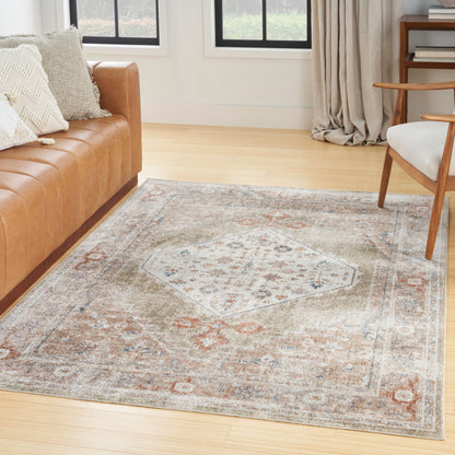 Muted vintage oriental rug with medallion in beige, blue, rust tones on light wood floor beside a tan leather sofa.