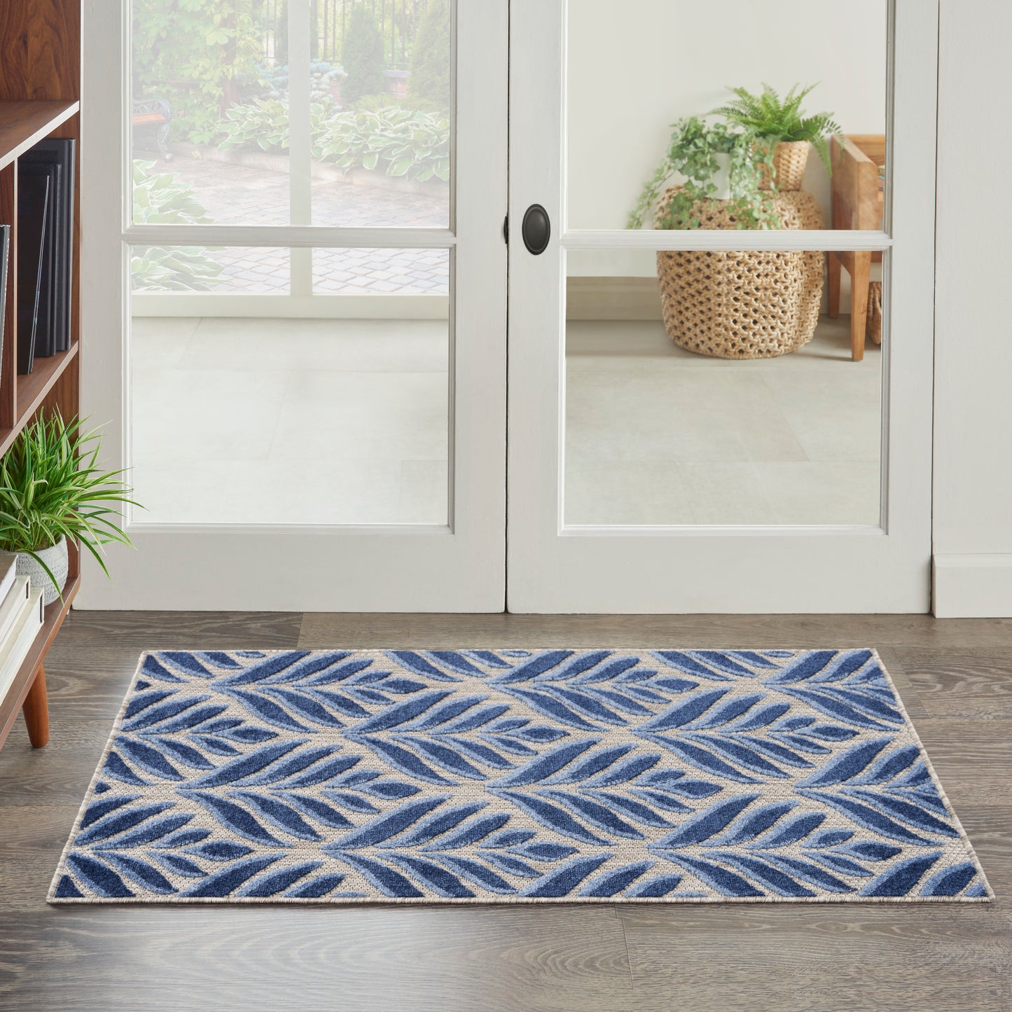 Blue and beige leaf-patterned rug on wood floor in front of white glass-paneled French doors; cozy entryway with plants.