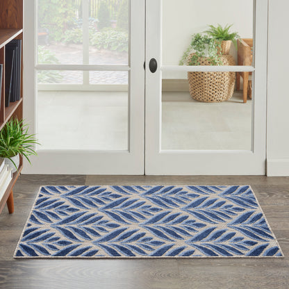 Blue and beige leaf-patterned rug on wood floor in front of white glass-paneled French doors; cozy entryway with plants.