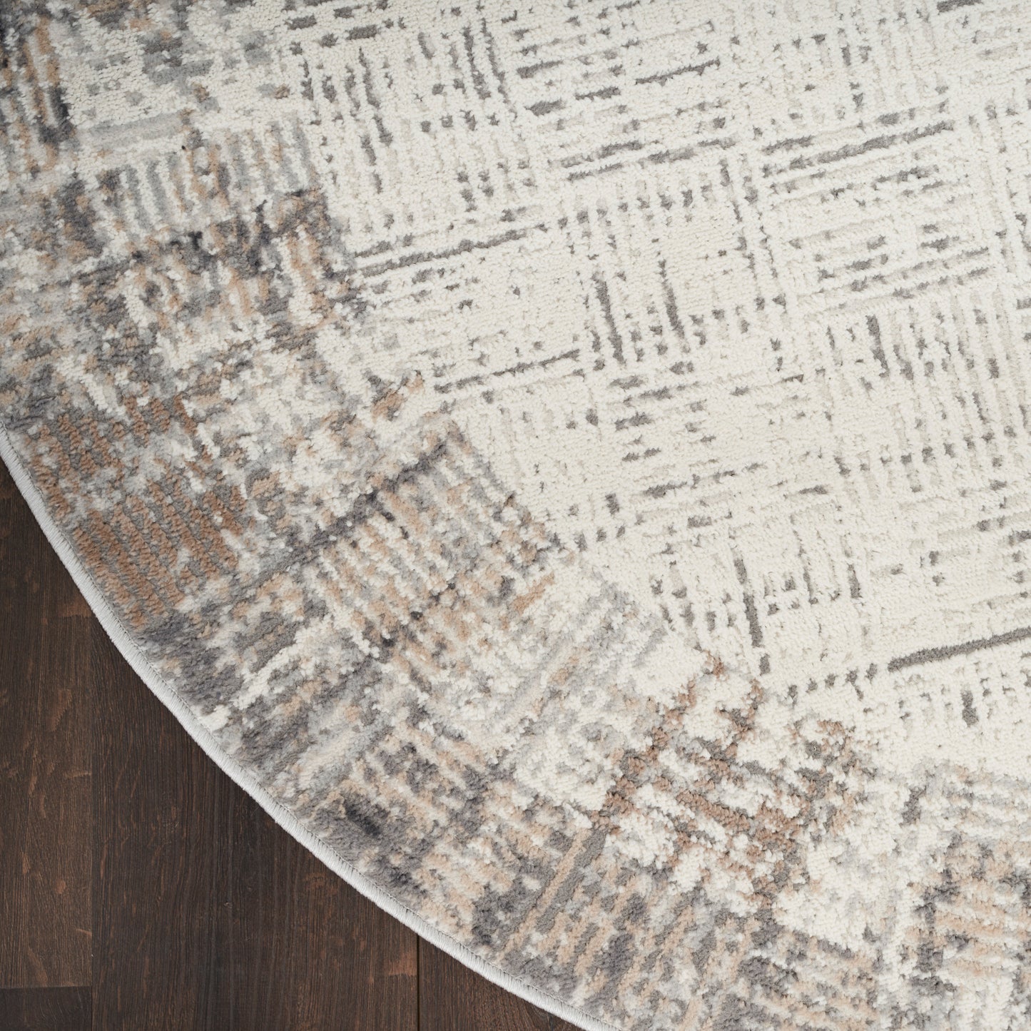 Abstract cream-gray rug with tan accents and curved edge on dark wood floor.