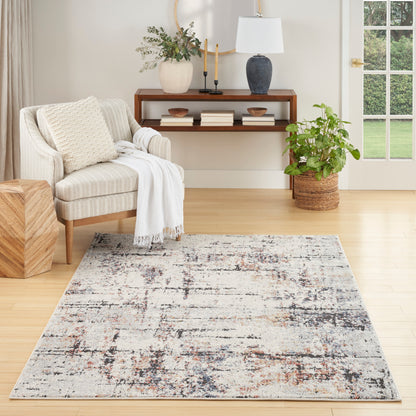 Neutral abstract area rug with cream, gray and charcoal tones on light wood floor beside a beige armchair and wooden console.