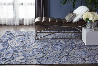 Blue-gray abstract-pattern rug under a brown leather chaise with a crisscross metal base in a modern living room.