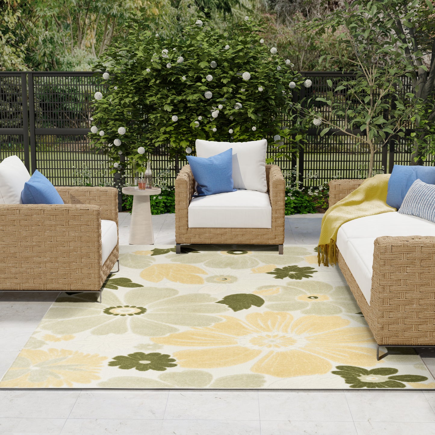 Outdoor wicker seating with white cushions, blue pillows on a pale yellow floral rug.