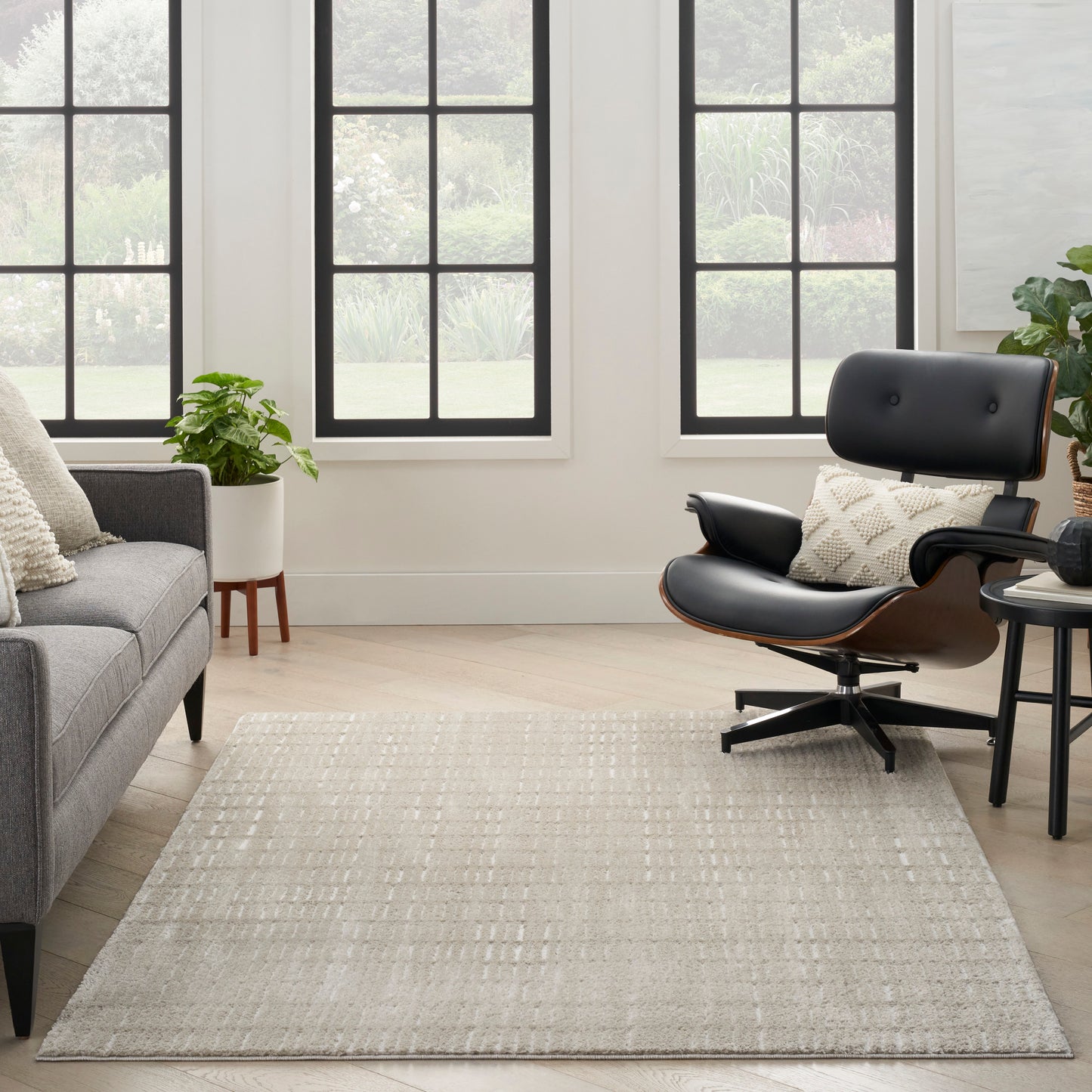 Light gray rectangular area rug with pale linear pattern in a modern living room beside a gray sofa and black leather lounge chair.