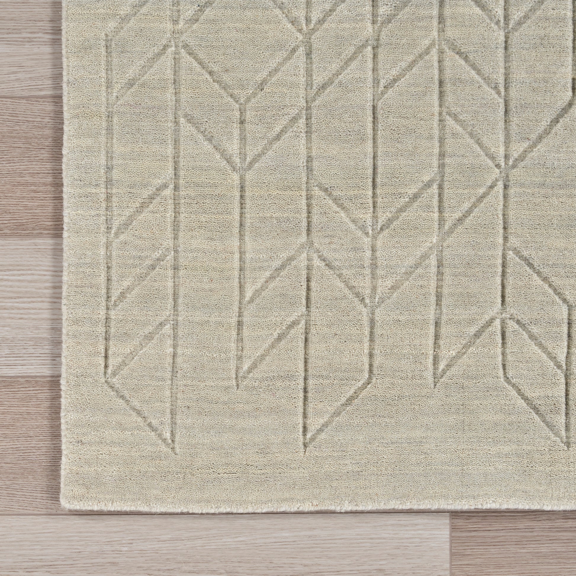 Beige woven area rug with geometric leaf and chevron pattern in light gray on a wooden floor.
