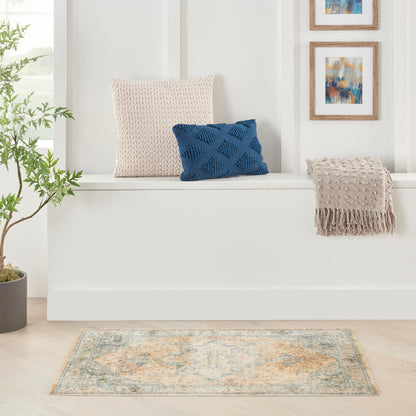 Beige knit pillow and navy blue diamond-pattern cushion on a white bench, beige fringed throw, plant, abstract art, and rug.