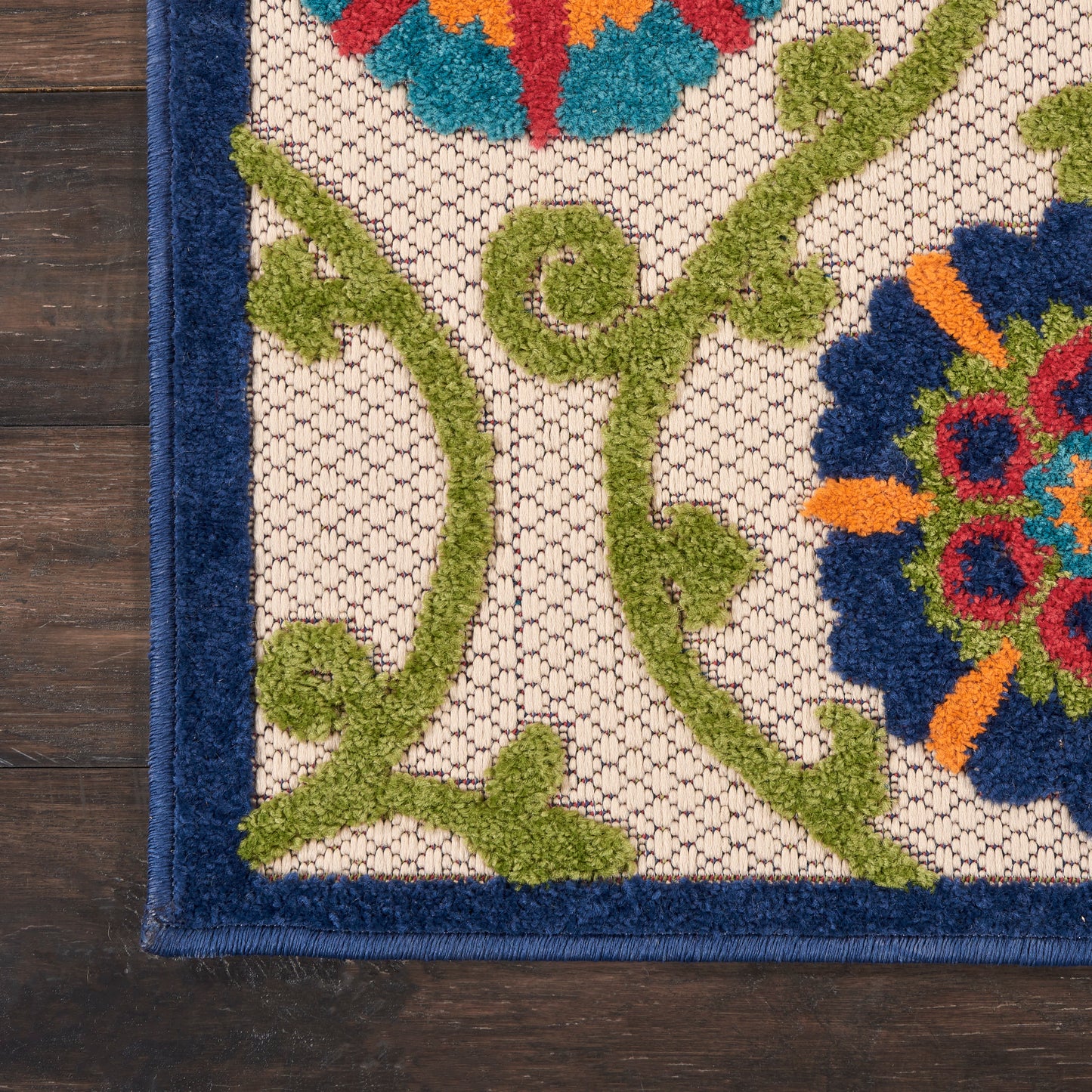 Decorative rug with green scrolling vines and bright multicolor floral medallions on beige lattice background, navy border.