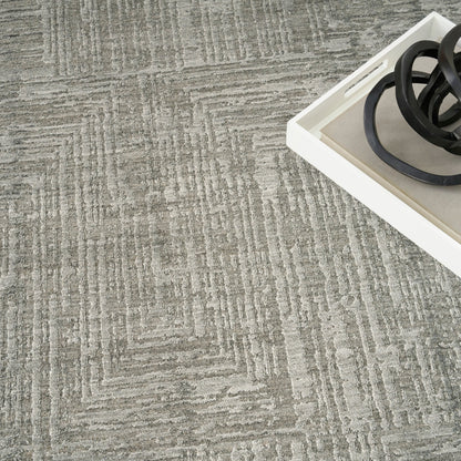 Gray geometric patterned area rug with raised texture; white tray in corner holds black circular rings.