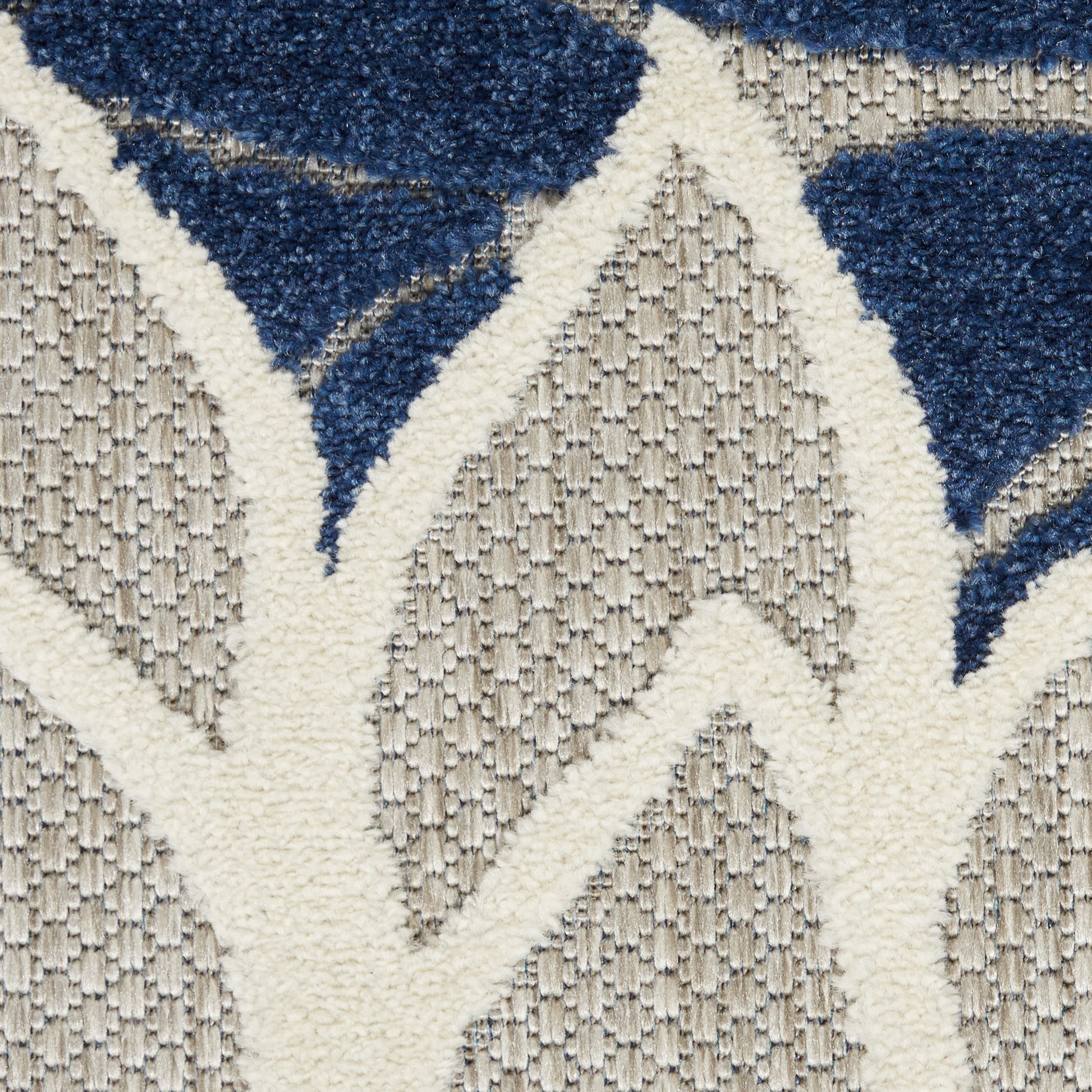 Close-up of a textured beige rug with an off-white lattice pattern and navy blue geometric shapes.