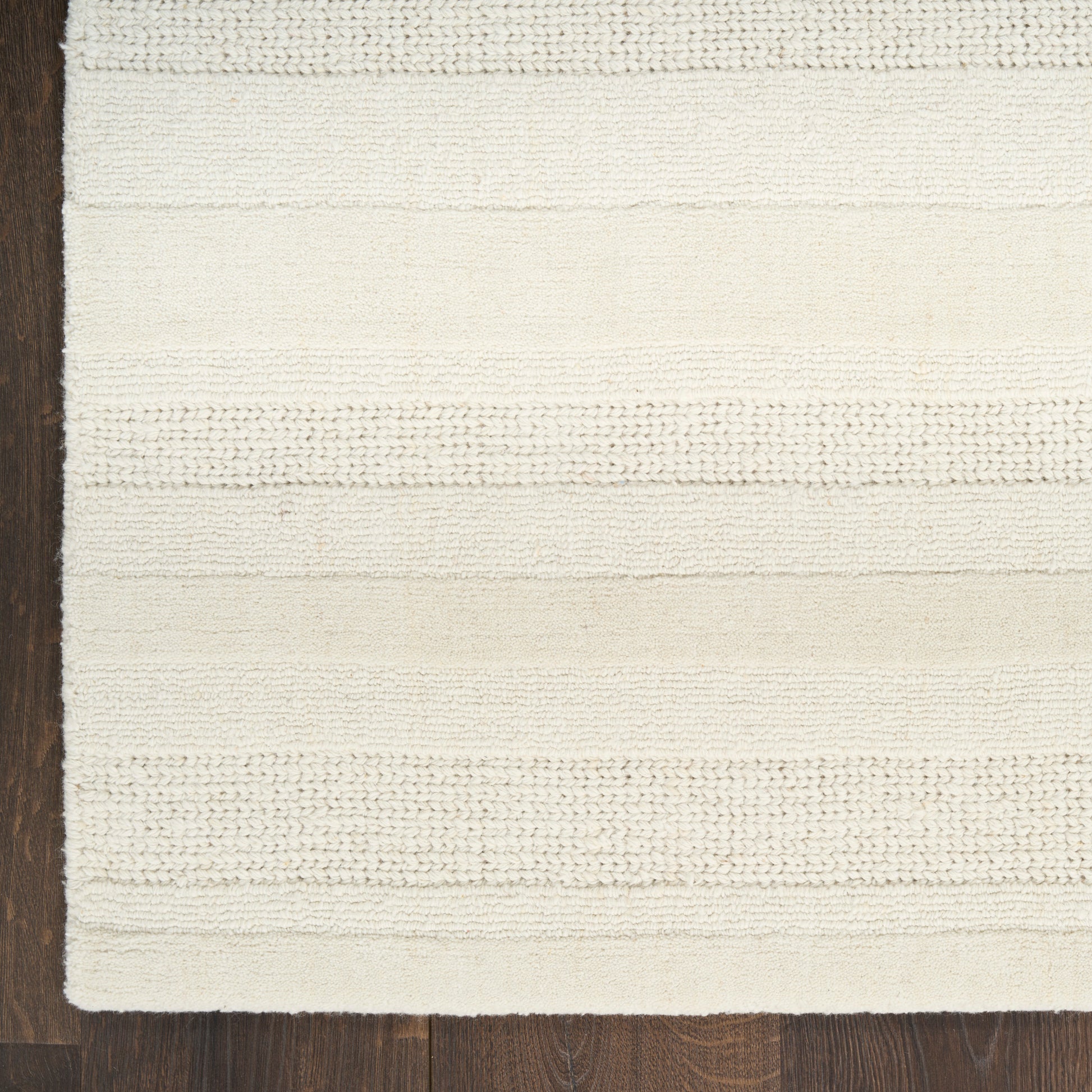 Cream rectangular rug with alternating knit stripes on dark wood floor; soft, woven texture.
