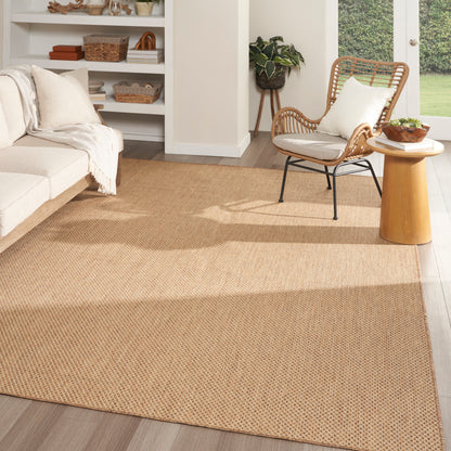 Natural beige jute rug in a bright living room with a wicker chair, white sofa, and wooden side table.