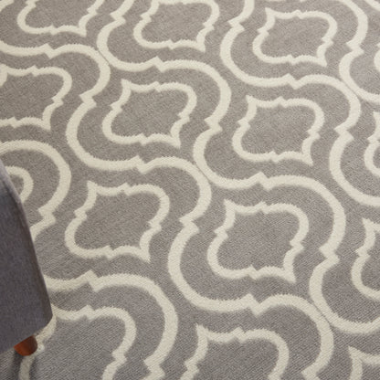Gray rug with white interlocking trellis motifs; soft woven texture, partial view of a wooden furniture leg.