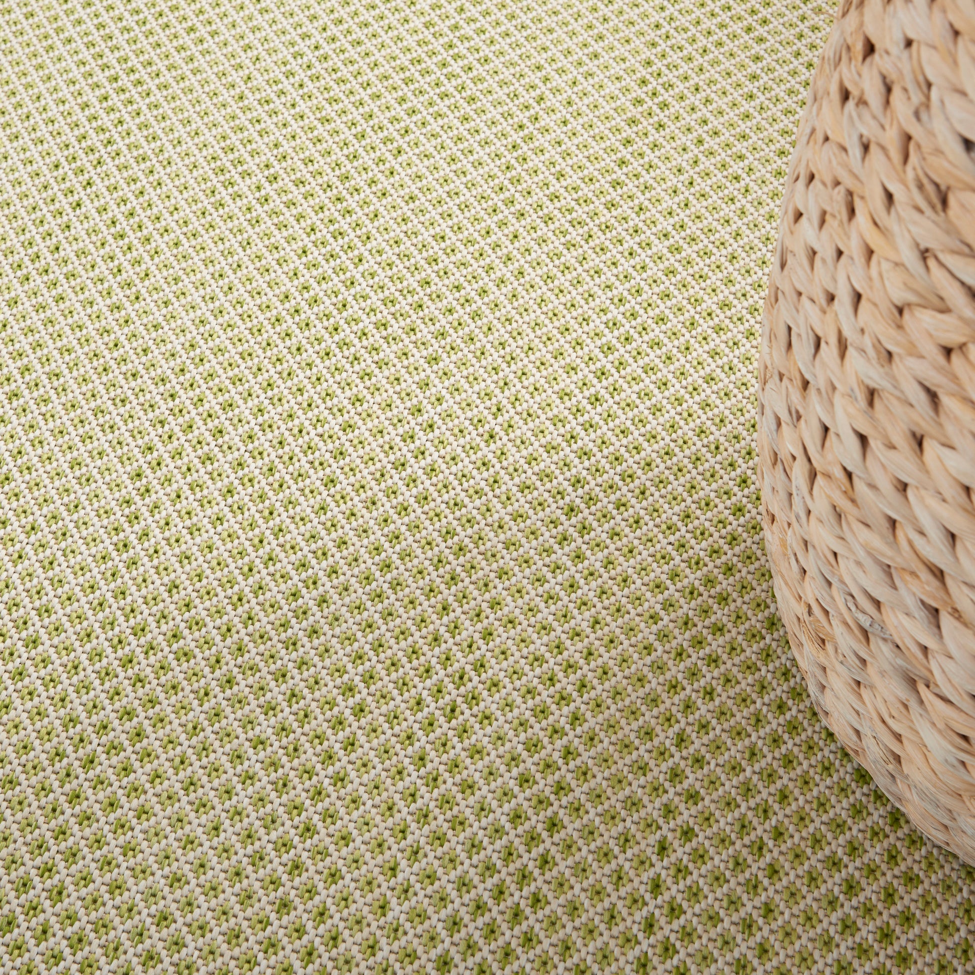 Natural beige woven straw basket with rounded sides on a pale green textured fabric backdrop.
