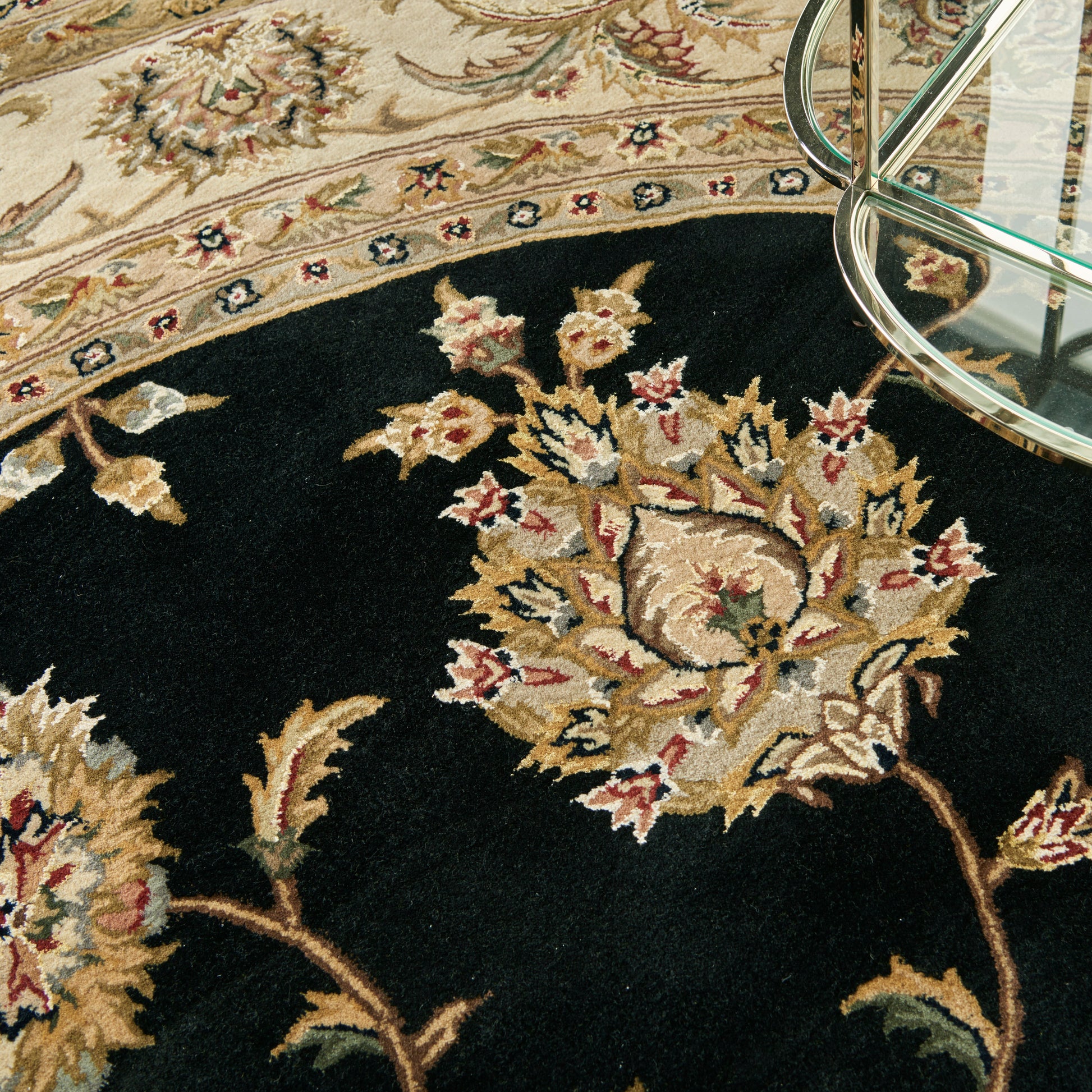 Ornate oriental rug with black field and cream-gold floral motifs, beige border; glass coffee-table leg visible.