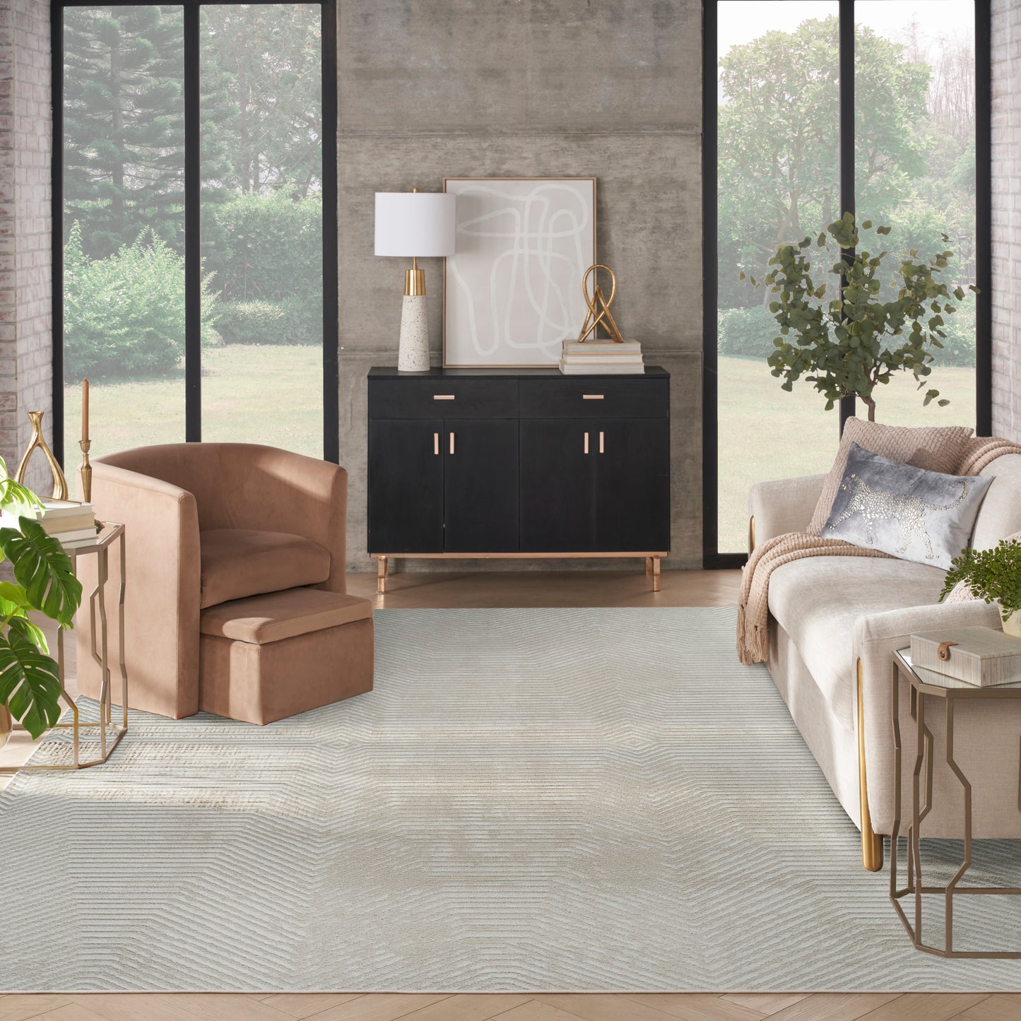 Contemporary living room with a rug, black sideboard, tan leather armchair & ottoman, cream sofa, gold accents, concrete wall.
