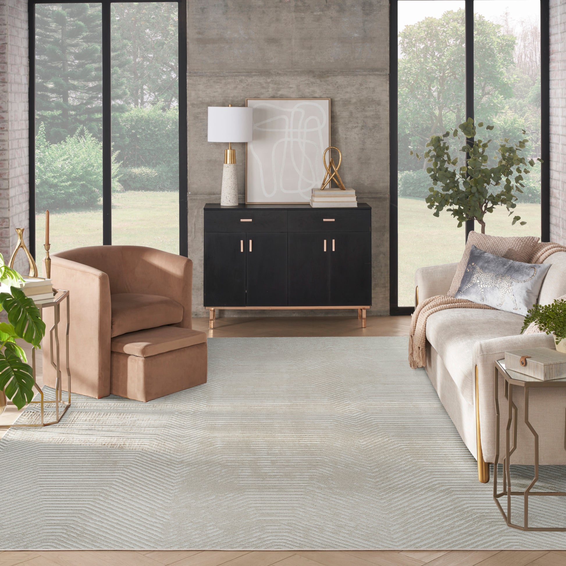 Contemporary living room with a rug, black sideboard, tan leather armchair & ottoman, cream sofa, gold accents, concrete wall.
