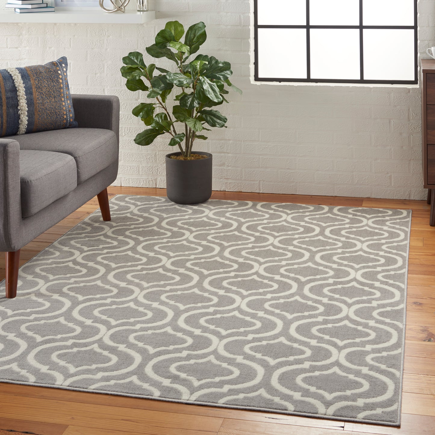 Grey and white trellis-pattern area rug in a modern living room with a grey sofa, potted plant, and large window.
