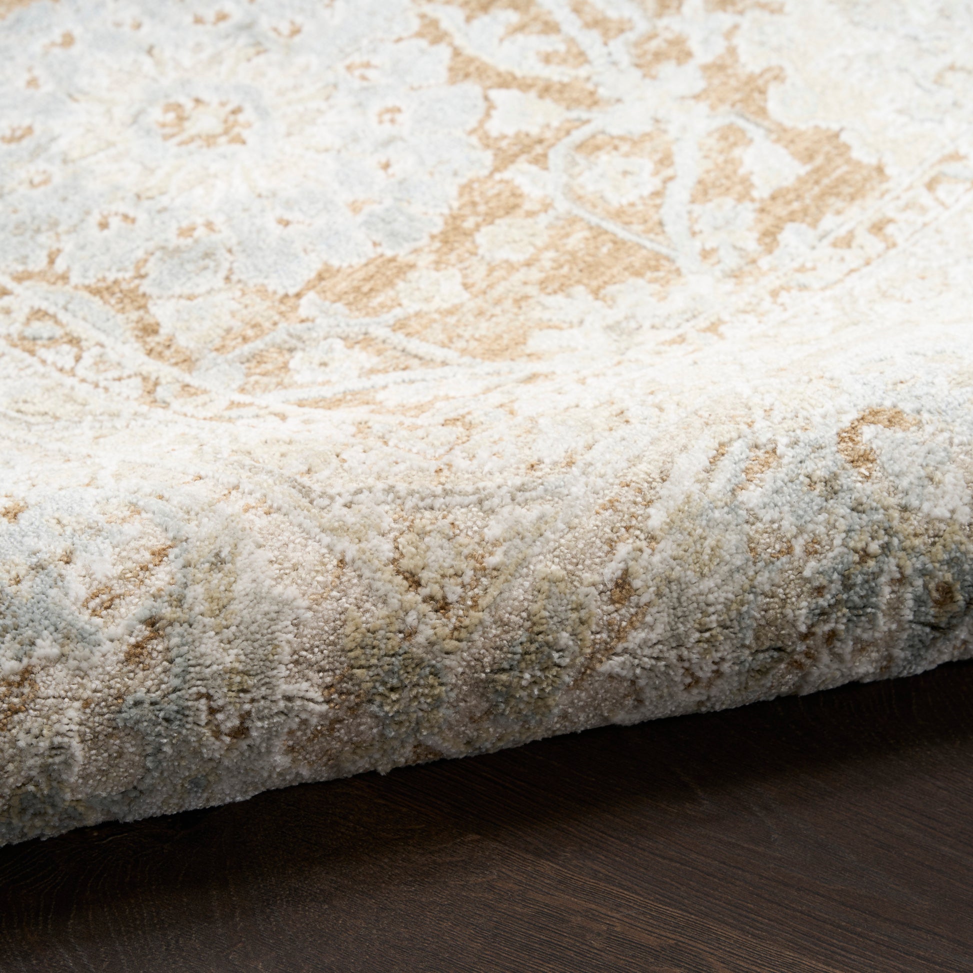 Cream and tan oriental rug with distressed floral motif, soft pile, curled edge on dark wood floor.