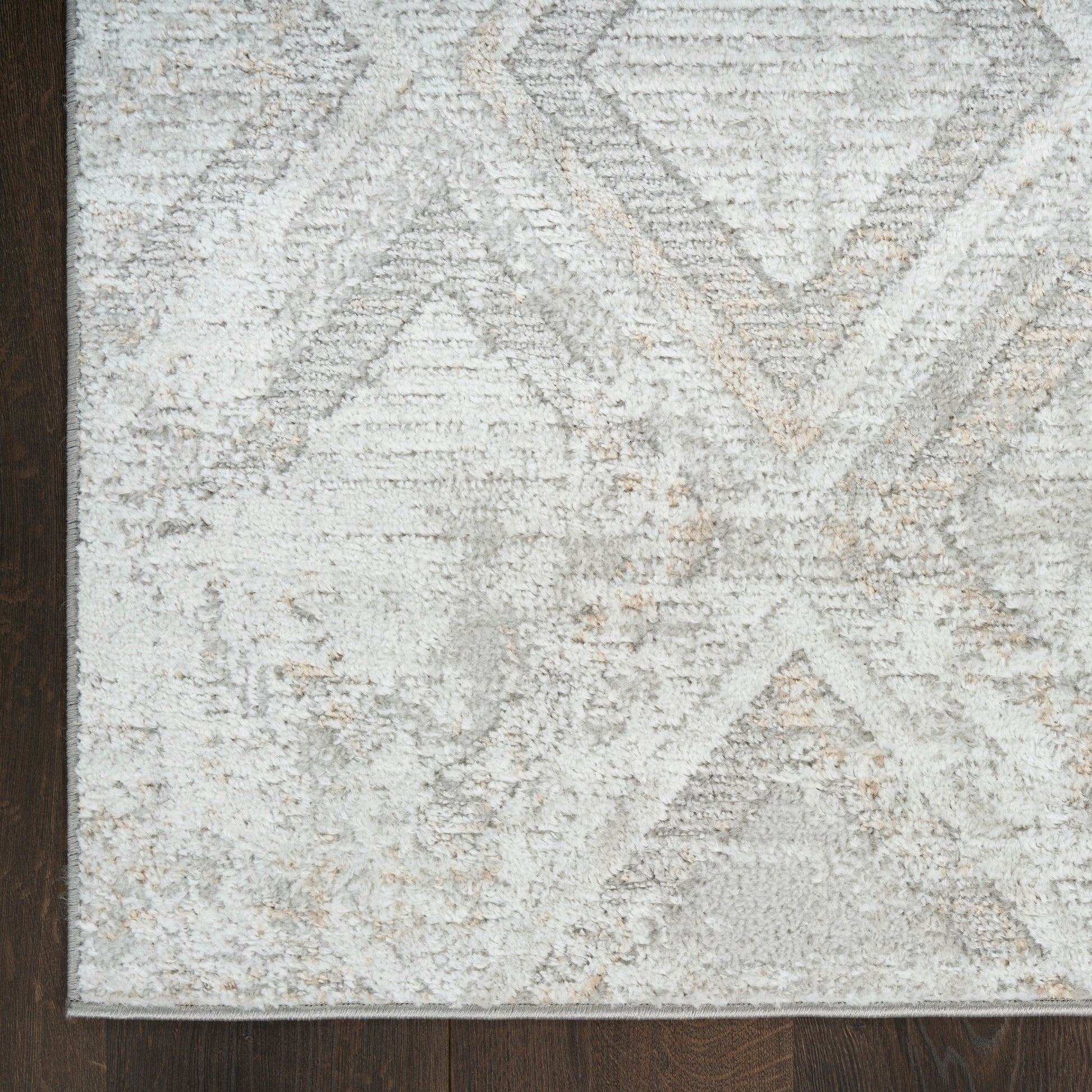 Light gray geometric area rug with diamond pattern and beige accents on dark wood floor.