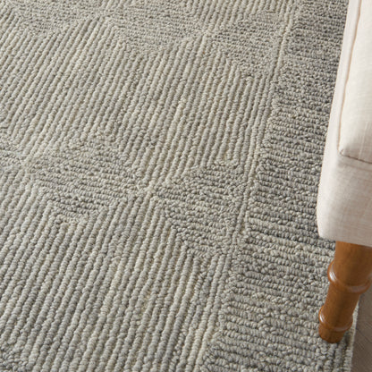 Gray textured area rug with raised loop pattern in circular and linear motifs, next to a light beige upholstered sofa leg.