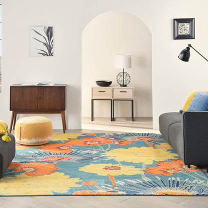 Living room with vibrant floral rug, mid-century furniture, yellow pouf, grey sofa, arched doorway, wood cabinet, floor lamp.