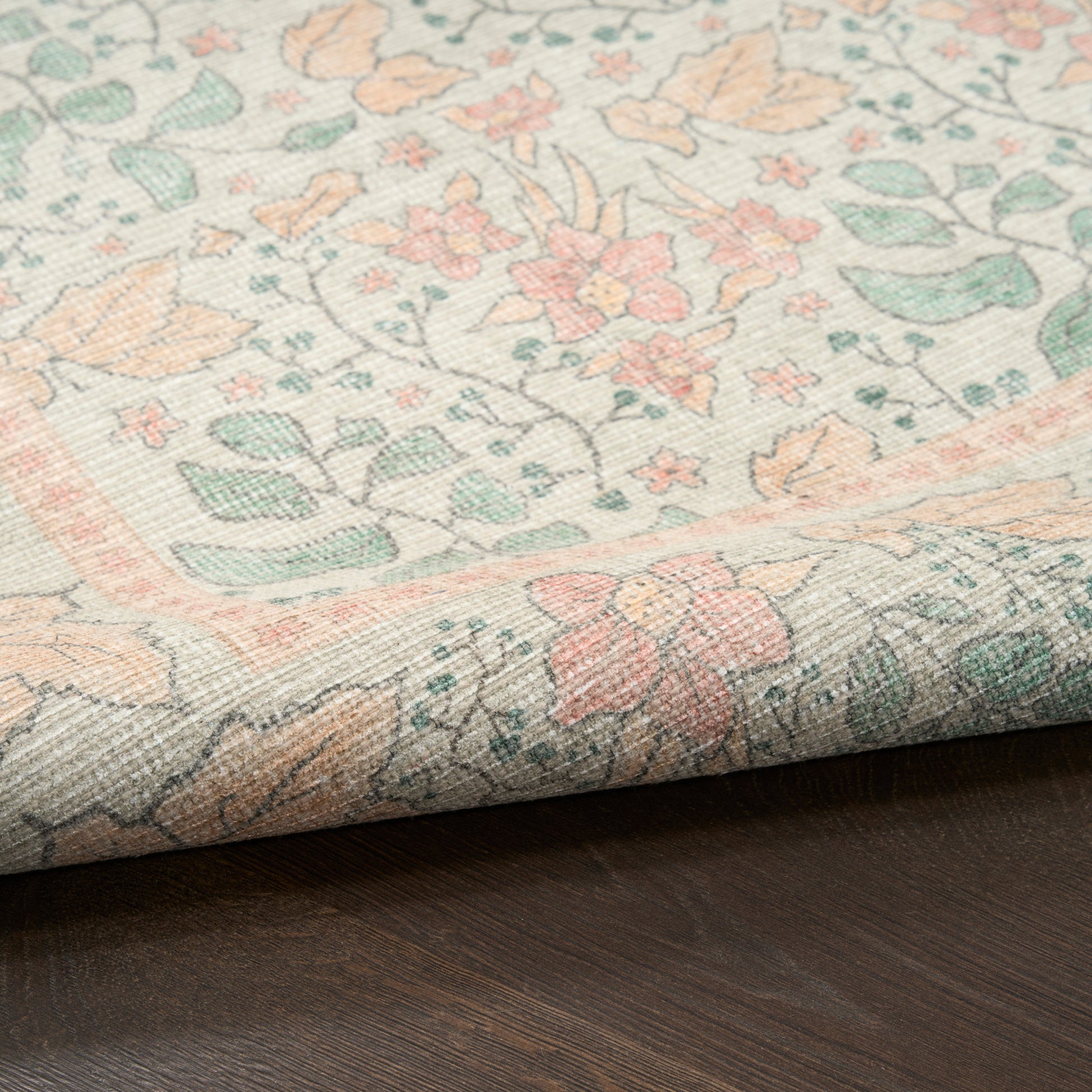 Pastel floral woven rug with ivory background, peach, mint and pink blossoms, folded edge on dark wood floor.