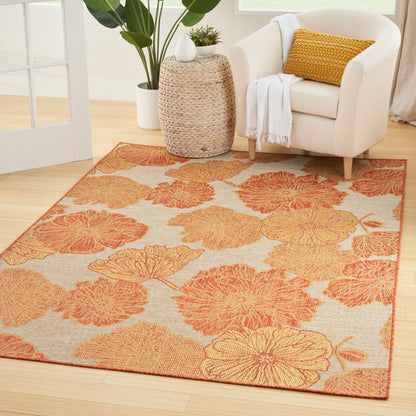 Indoor living room rug with orange floral pattern on beige background; paired with cream armchair and woven side table.